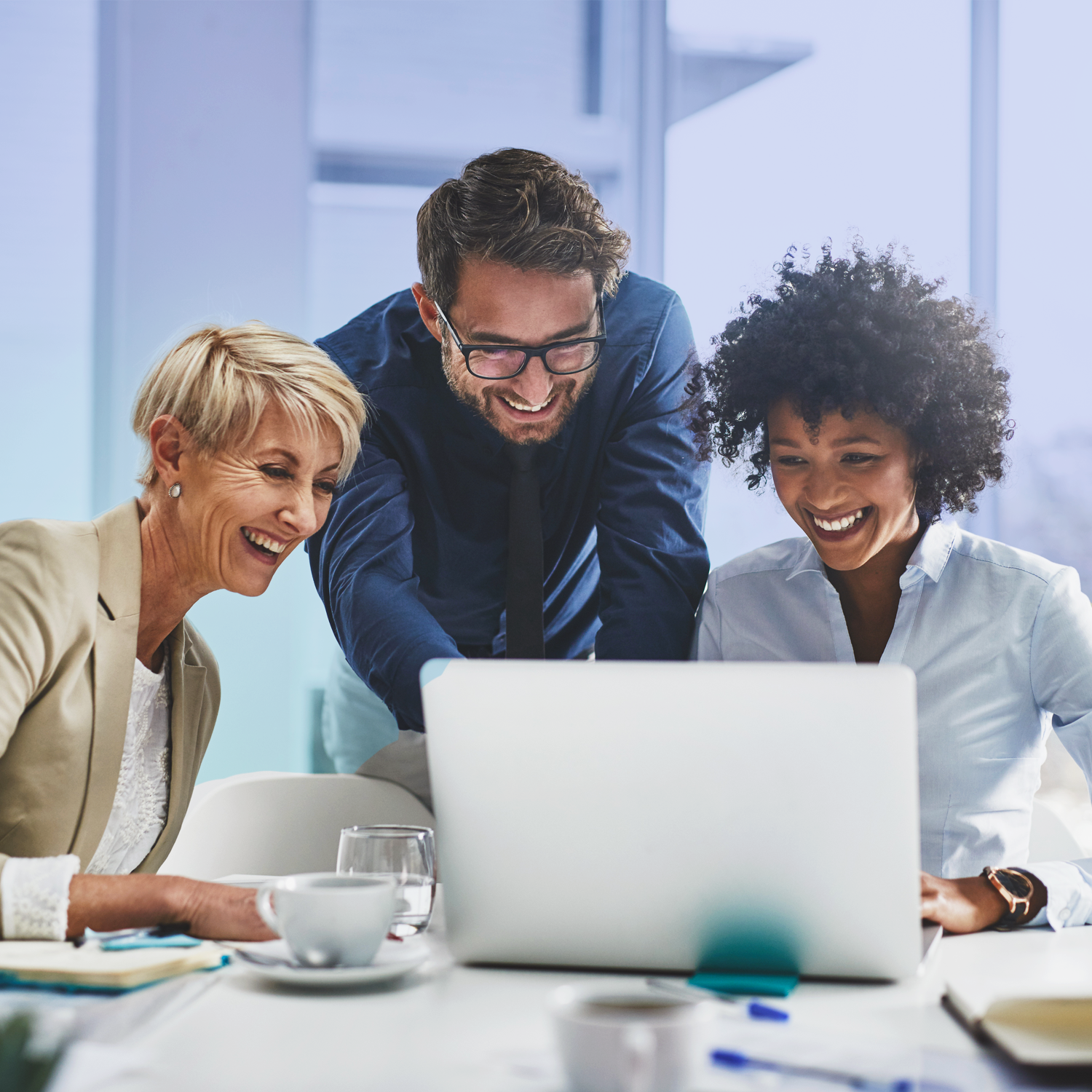 Three professionals, two women and a man, look at a laptop screen. They're all smiling.