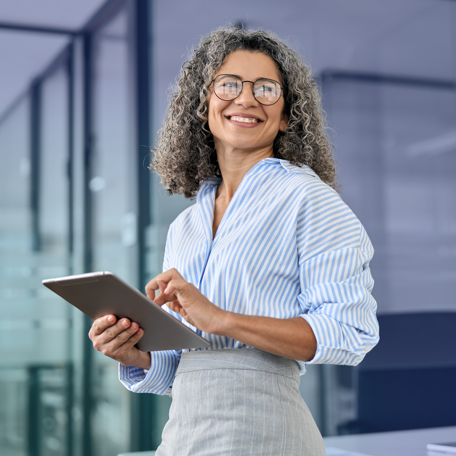 Happy professional woman wearing glasses is wearing a striped business shirt and touching a tablet at work.